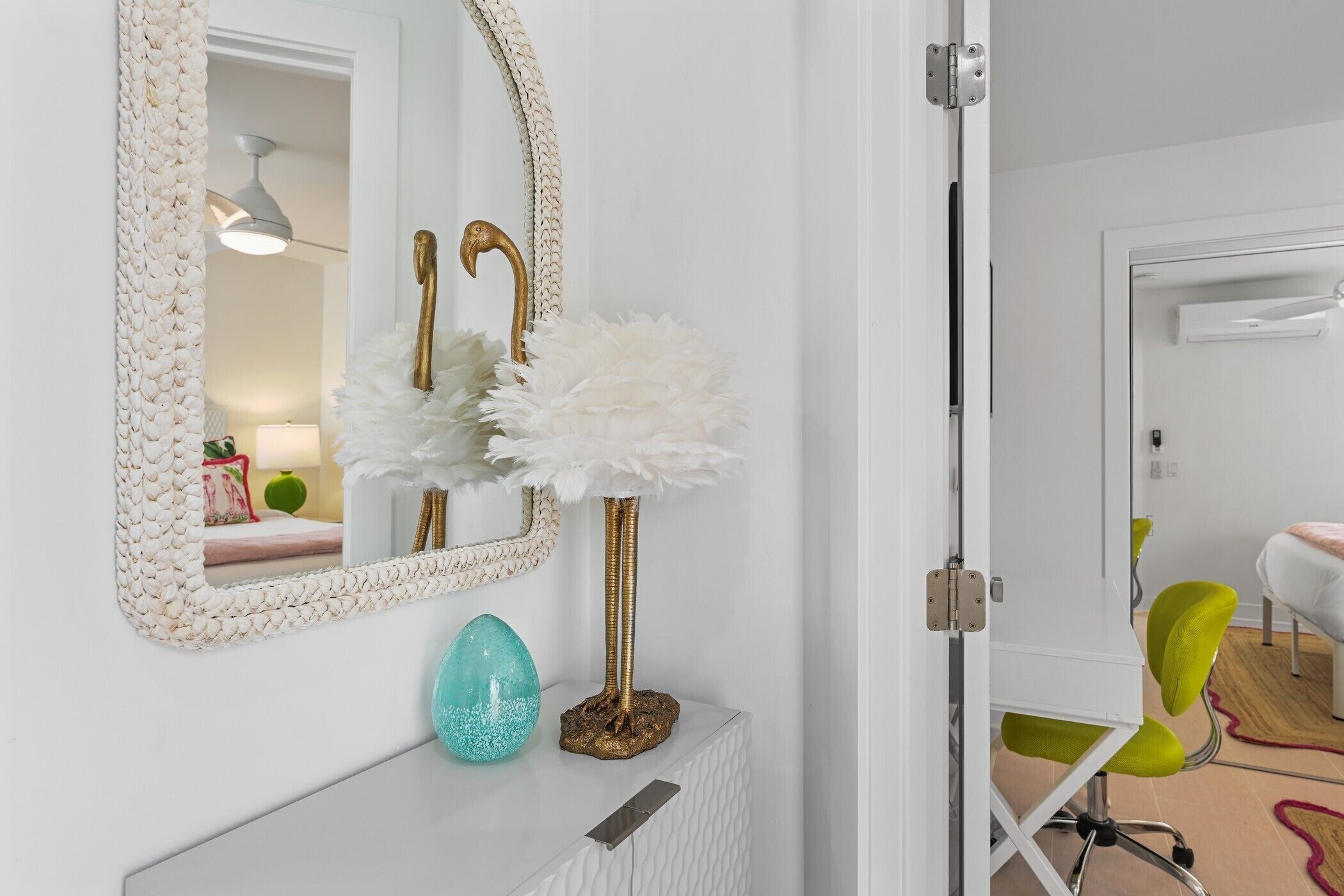 Une console blanche agrémentée d’un miroir décoratif, d’une lampe dorée et d’un vase turquoise.
