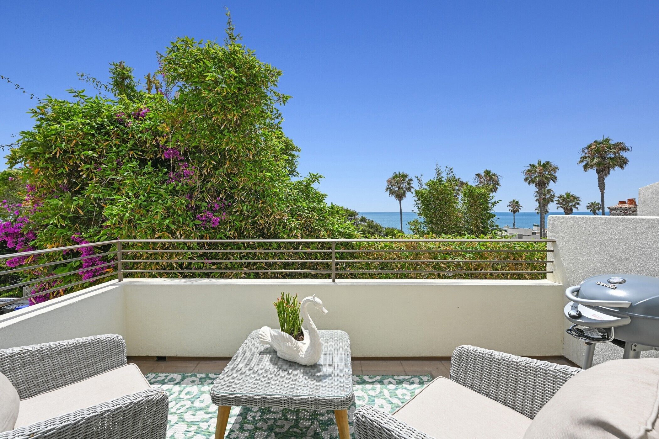 A balcony with wicker furniture, a swan-shaped planter, and a barbecue grill.
