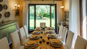 A dining room with a table set for six, featuring a view of a garden through large windows. - Dolce Collina 10, Emma Villas (Cesena)