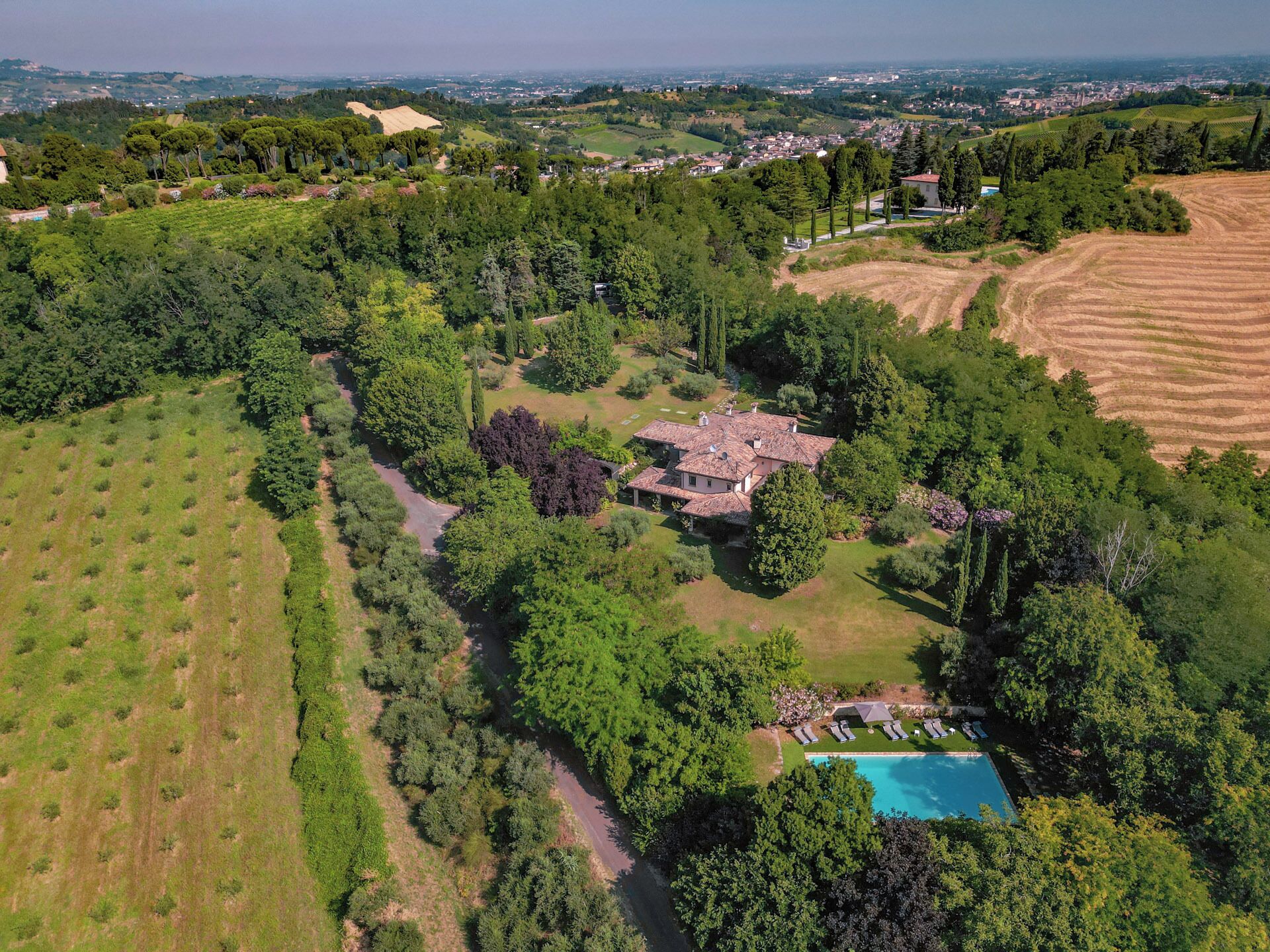 Vista aérea de una propiedad con una casa grande rodeada de abundante vegetación, una piscina y campos en terrazas.