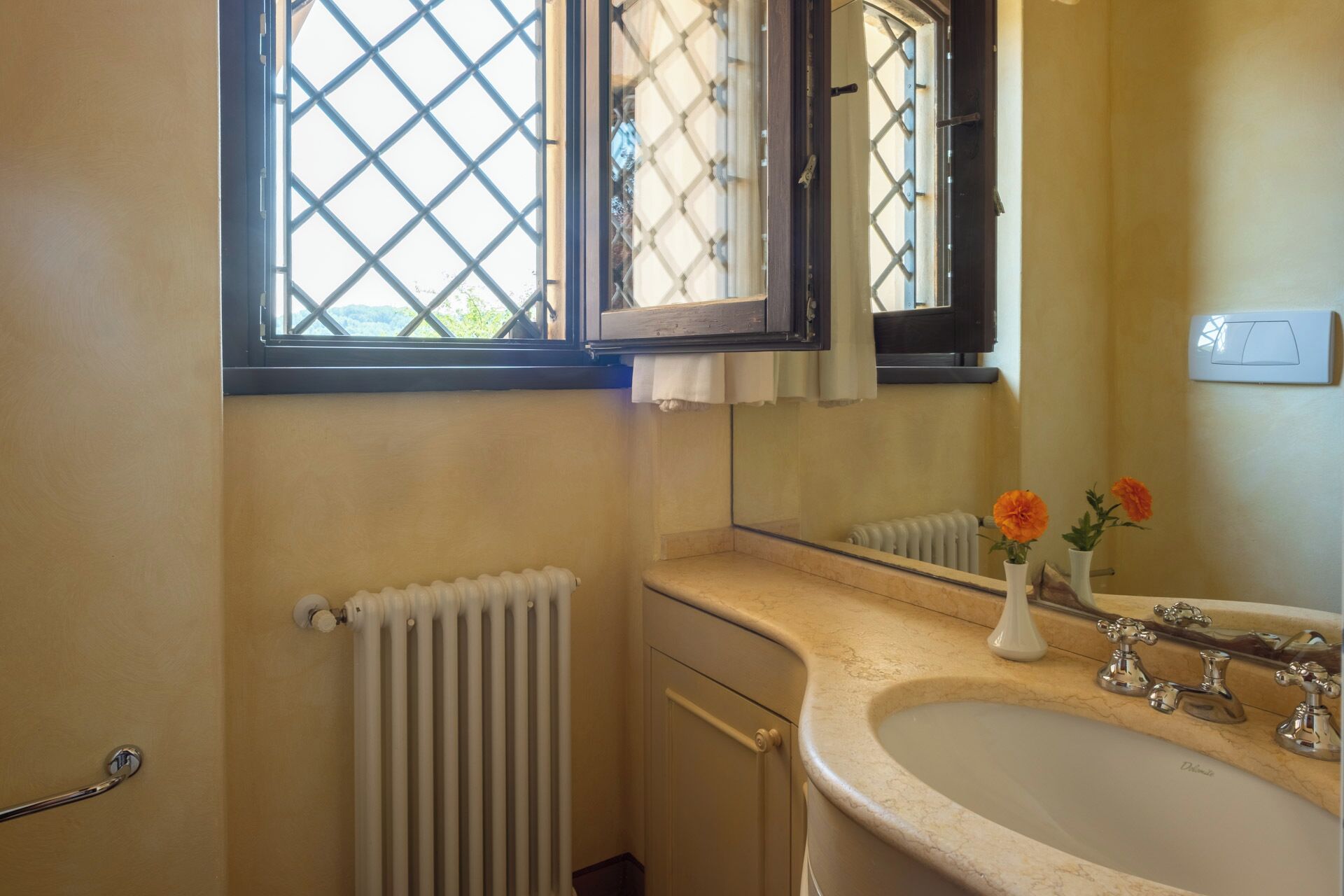 A bathroom with a white sink, a mirror, and a window with a lattice design.