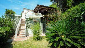 A house with a stone staircase leading to a wooden deck, surrounded by lush greenery and a palm tree. - Villa La Pigrizia - One Bedroom Villa, Sleeps 2 (Forio)