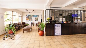 A reception area with a wooden reception desk, seating area with chairs and tables, potted plants, and a large window. - Hotel Costa del Sol (Puerto Vallarta)