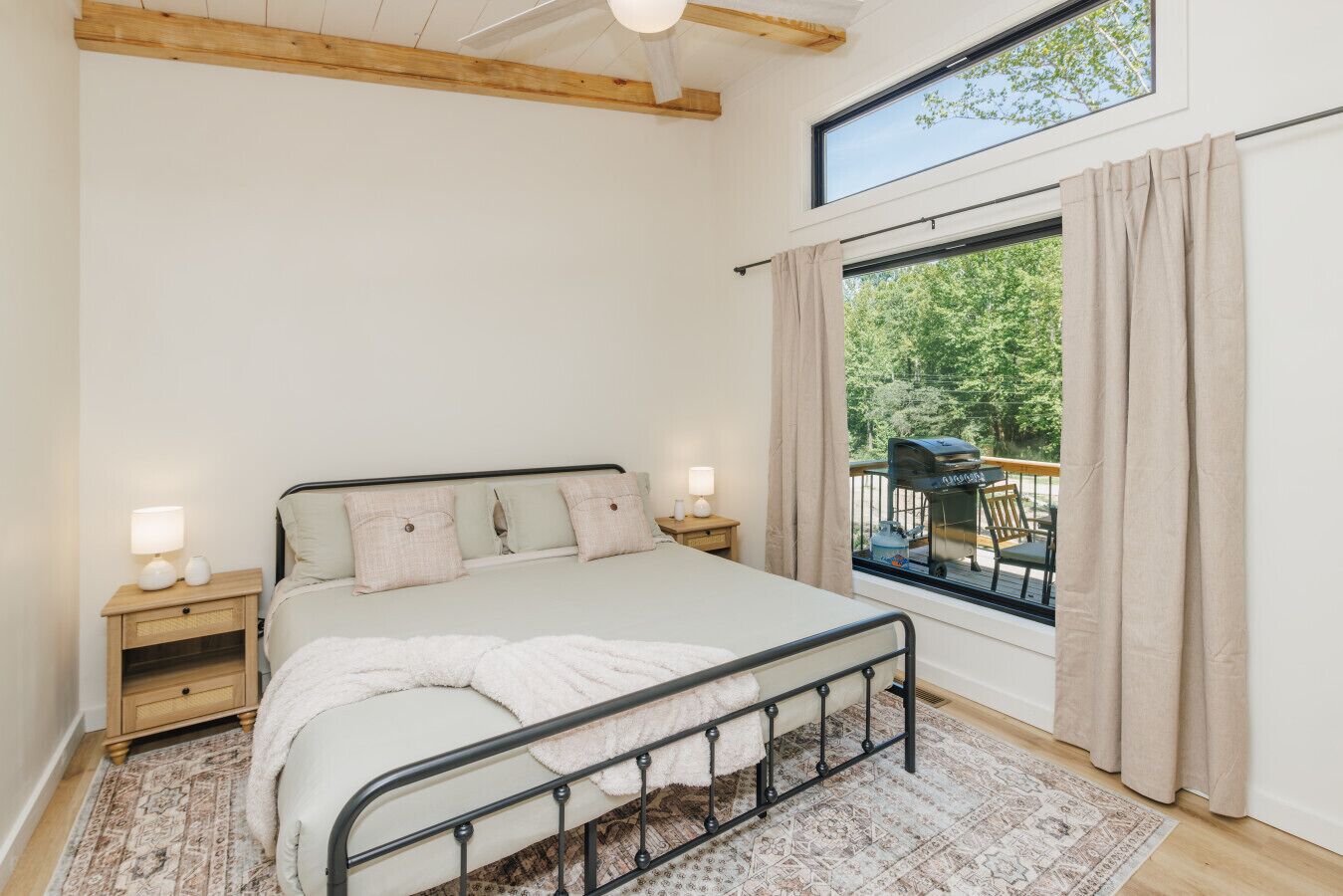 A bedroom with a bed, bedside tables, a window with curtains, and a view of the outdoors.