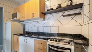 Una cocina con armarios de madera, estufa a gas, horno empotrado, refrigerador y microondas sobre una estantería.