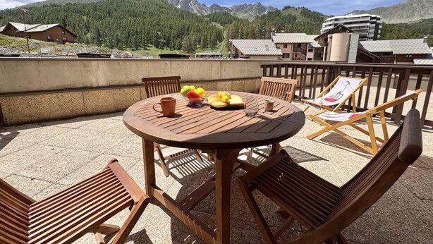 Ein runder Holztisch mit Stühlen, einer Obstschale und einer Tasse auf der Terrasse mit Blick auf die Berge.