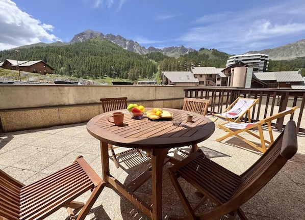 Ein runder Holztisch mit Stühlen, einer Obstschale und einer Tasse auf der Terrasse mit Blick auf die Berge.
