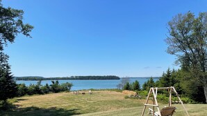 Un espace verdoyant avec une balançoire, un foyer et une vue sur un lac et des arbres au loin.