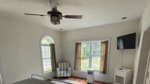 Une chambre à coucher avec un lit, une chaise, un téléviseur et un ventilateur de plafond.