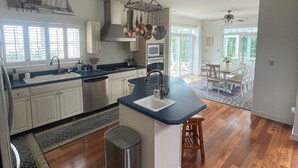 Une cuisine spacieuse dotée d’un îlot central, un coin repas avec une table et des chaises, et une vue sur l’extérieur grâce à de grandes fenêtres.