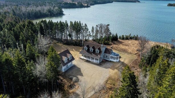Une grande maison avec un garage et une véranda, entourée d’une forêt dense et d’un lac.