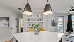 A modern kitchen with a central island, pendant lights, a bookshelf, and a television. - Stylish & Clean Oasis | City Center | Pool & Gym (Tampa)