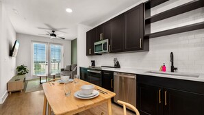 A modern kitchen with dark cabinets, a microwave, and a dishwasher. There is a dining table with chairs and a small plant.
