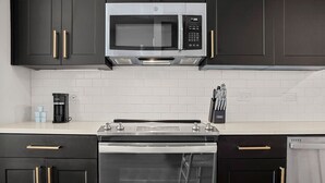 A kitchen with dark cabinets, a stainless steel microwave, a built-in oven, and a coffee maker on the counter. - Charming 1-Bedroom | Close to Raymond James! (Tampa)