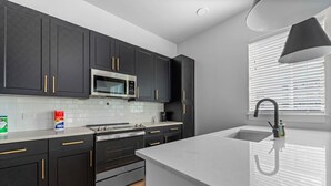 A modern kitchen with dark cabinetry, a stainless steel microwave, and a large island with a sink.