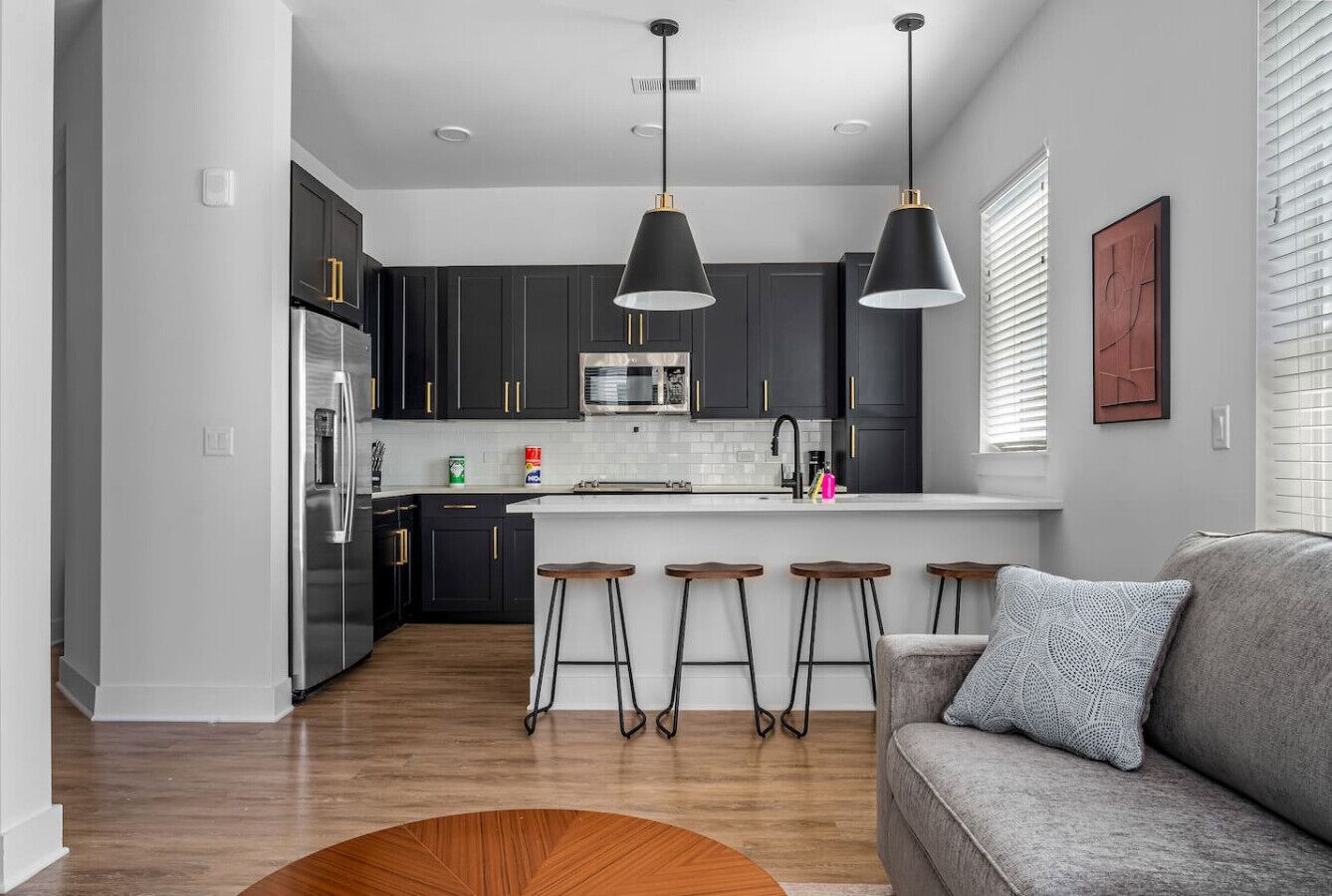 A modern kitchen with dark cabinets, stainless steel appliances, and a central island with stools.