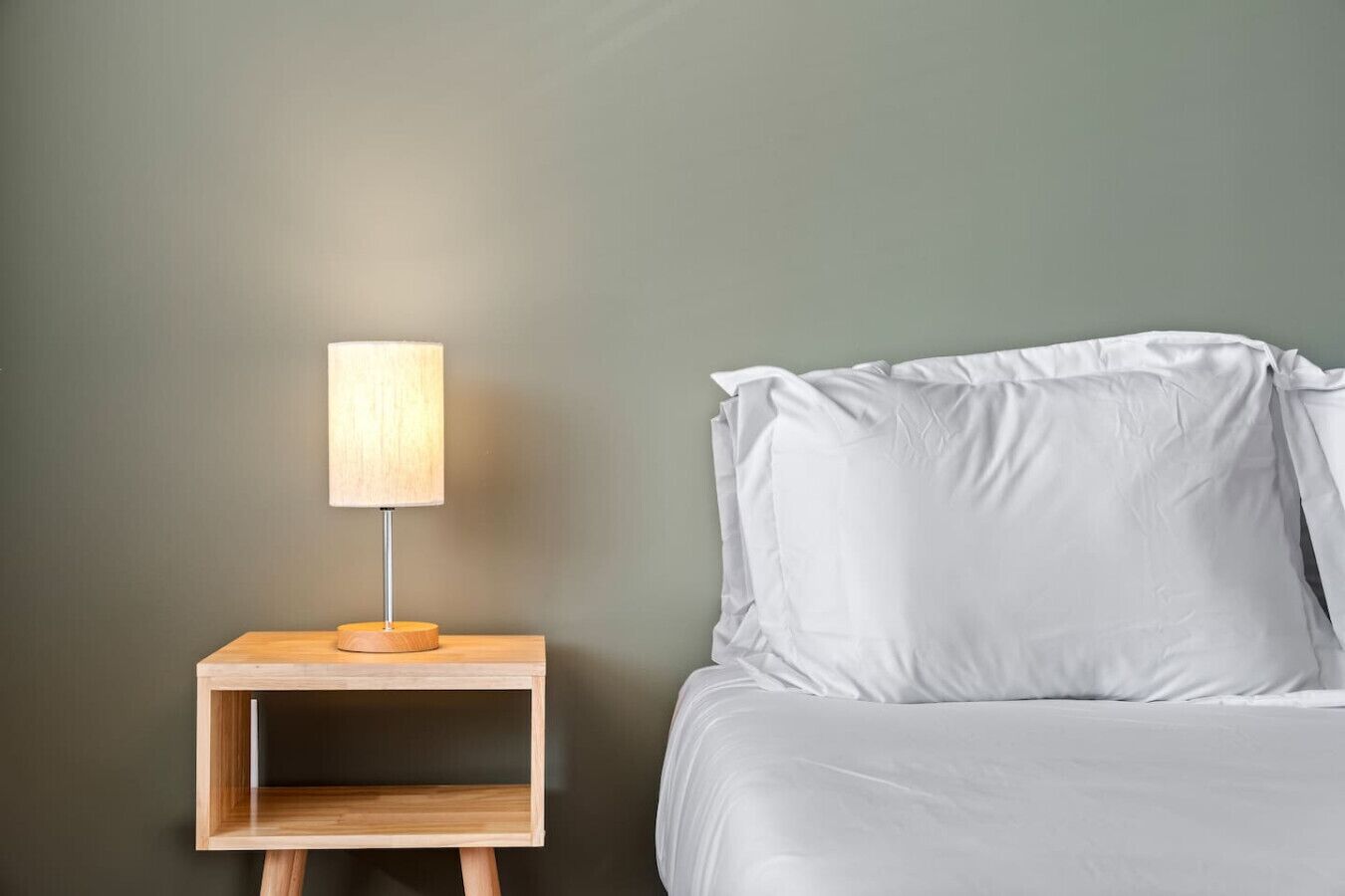 Una cama con ropa de cama blanca y una mesita de noche con una lámpara.