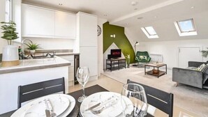 A modern apartment with a kitchen, dining area, living room, and a loft bedroom with skylights.