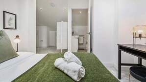 A modern hotel room with a neatly made bed, a green area rug, a bedside table with a lamp, and a view into the bathroom.