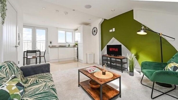 A modern living room with a green accent wall, a sofa, a coffee table, and a TV displaying 'NETFLIX'.