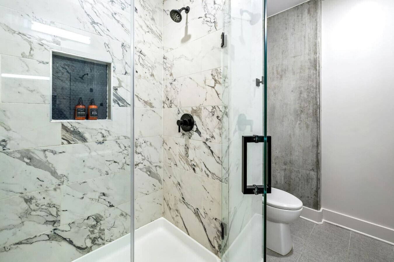 Une salle de bain moderne avec une douche à parois de verre, des toilettes et un mur recouvert de carreaux de marbre.