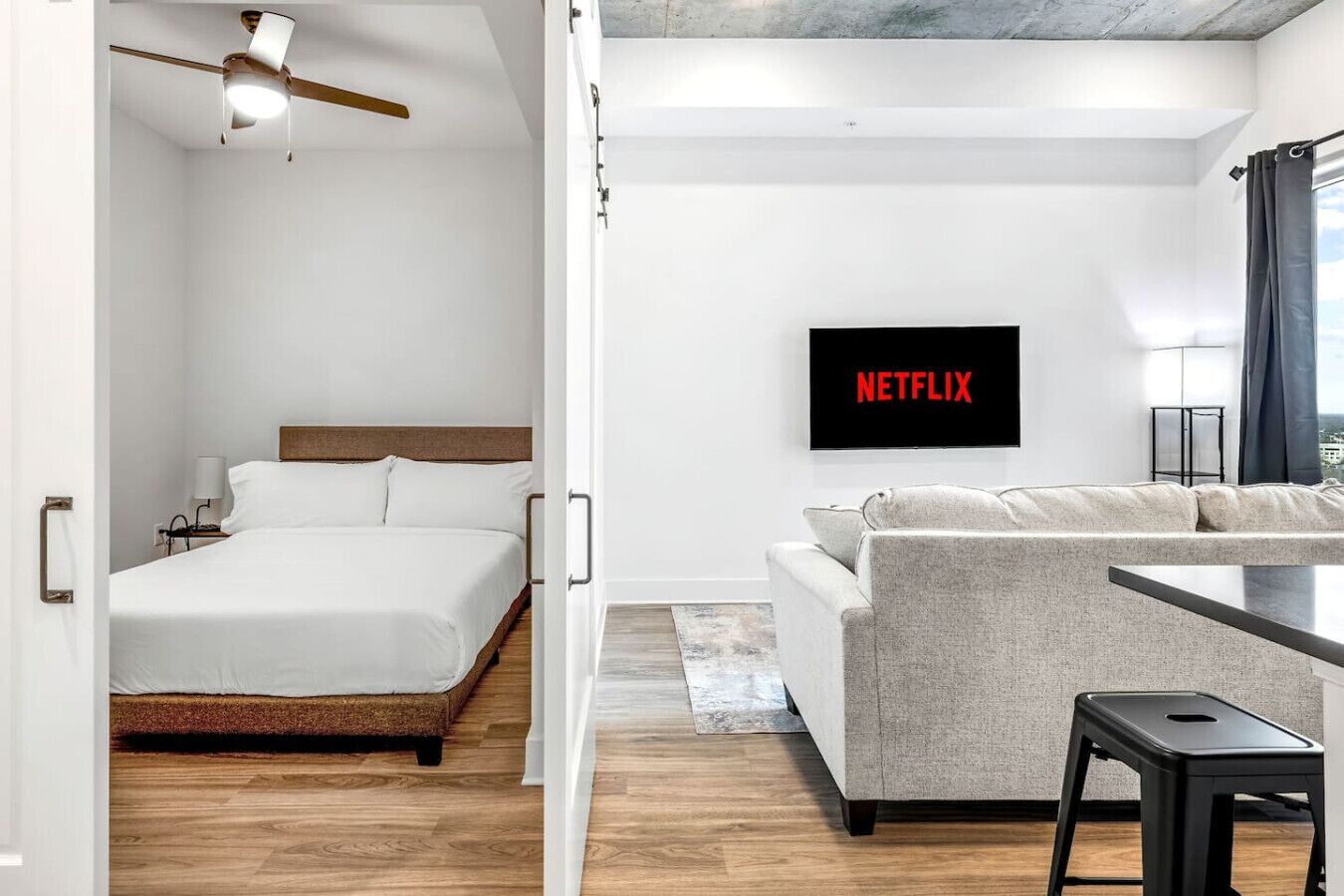 A modern hotel room with a bed, a sofa, a TV mounted on the wall, and a ceiling fan.
