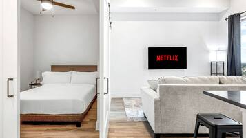 A modern hotel room with a bed, a sofa, a TV mounted on the wall, and a ceiling fan.