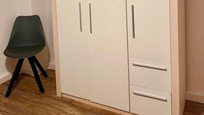 Un armari blanc amb dues portes i una prestatgeria, una cadira verda i un sòl de fusta.