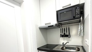 Una cuina compacta amb armaris blancs, tauleig negre, microones integrat i rentavaixelles.
