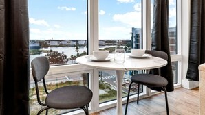 Une chambre moderne dotée d’une grande fenêtre, d’une table ronde avec des chaises, et offrant une vue sur un pont et sur l’eau.