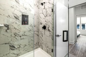 A modern bathroom with marble tiles, a glass shower enclosure, and a white bathtub. - The Perfect 2BD in Channelside District! (Tampa)