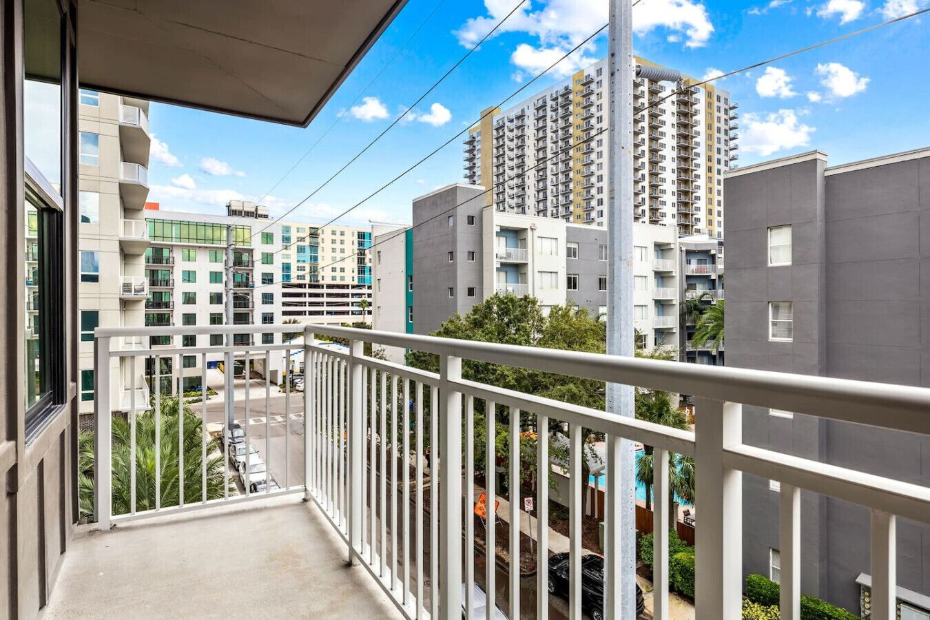 Een balkon met uitzicht op moderne appartementen, een heldere lucht en een straat eronder.