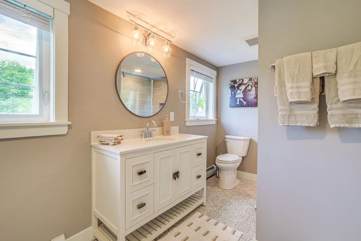 Une salle de bain avec un meuble-lavabo blanc, un miroir rond, des toilettes et un porte-serviettes.