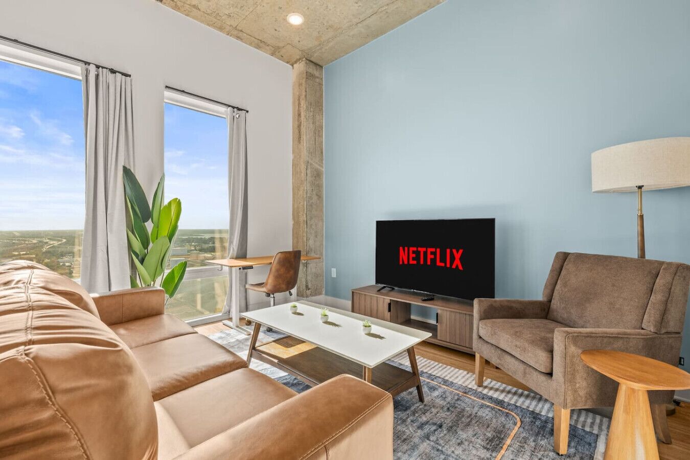 A modern living room with a sofa, armchair, coffee table, and a TV displaying 'NETFLIX'.