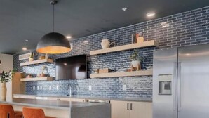 A modern kitchen with a brick backsplash, stainless steel appliances, and orange bar stools.