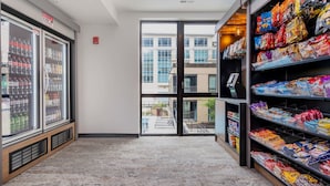 A grocery store interior with refrigerated beverage cases, snack shelves, and a view through the door to the outside.