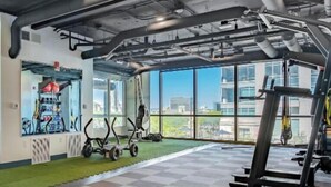 A gym with exercise equipment, large windows, and a view of buildings. - Central Indy 1BD Stay • Fee Parking+Pool & Gym (Indianapolis)