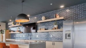 Una cocina moderna con salpicadero de ladrillo, electrodomésticos de acero inoxidable y taburetes de bar naranja.