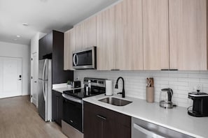 Una cocina moderna con armarios oscuros, electrodomésticos de acero inoxidable, microondas y cafetera.