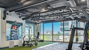 Une salle de sport équipée de matériel d’exercice, dotée de grandes fenêtres et offrant une vue sur les bâtiments.