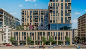 Un immeuble moderne à plusieurs étages, doté d’une façade plate, de grandes fenêtres et d’un mélange de balcons et d’espaces commerciaux situés au niveau du rez-de-chaussée.