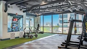 A gym with exercise equipment, large windows, and a view of buildings. - Super LUX High-Rise: Free Espresso+Pool+Gym+Lounge (Indianapolis)