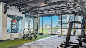 A gym with exercise equipment, large windows, and a view of buildings.