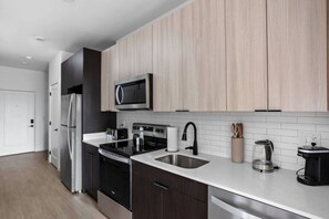 Una cocina moderna con armarios oscuros, electrodomésticos de acero inoxidable, microondas y cafetera.