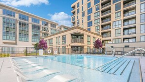 Una piscina con sillas de descanso, rodeada por un edificio con varios balcones y amplias ventanas.