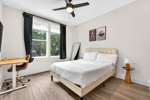 Quarto com cama, escrivaninha, cadeira, ventilador de teto e obras de arte na parede.