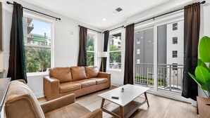 A modern living room with a sofa, armchairs, a coffee table, and large windows with curtains. - Upscale 2BR Stay | Minutes from Convention Center (Tampa)