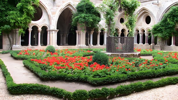 Un patio con una fuente, rodeado de arcos y flores rojas.
