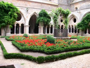 Une cour avec une fontaine, entourée d’arcades et de fleurs rouges.