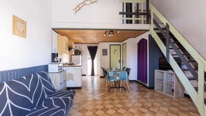 Amplia sala de estar con sofá, mesa de comedor, escalera y zona de cocina.